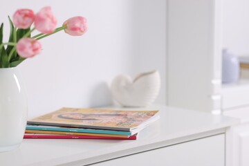 Many different trendy magazines and tulip flowers on white cabinet indoors, closeup