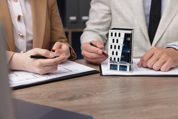 Real estate agent working with client at desk with house model in office, closeup