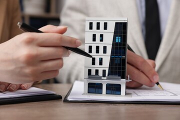 Real estate agent working with client at desk with house model in office, closeup