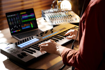Man working with MIDI keyboard at wooden table indoors, closeup