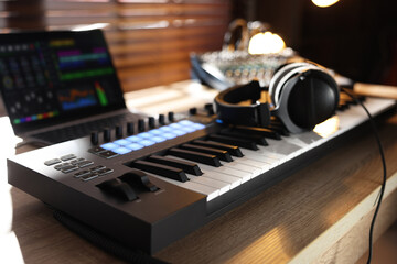 MIDI keyboard with headphones, laptop and dj mixer on wooden table indoors, closeup