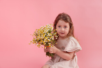Cute little girl with bouquet of beautiful chamomile flowers on pink background