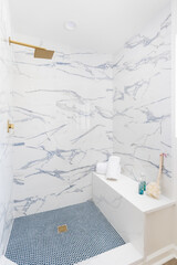 A styled, luxury shower with calacatta marble tiled walls, blue circular tile flooring, gold shower...