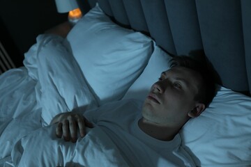 Frustrated man suffering from insomnia in bed indoors