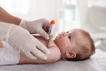 Pediatrician examining baby with thermometer at table in clinic, closeup