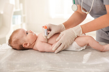 Pediatrician examining baby with thermometer at table in clinic, closeup