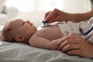 Pediatrician examining baby with stethoscope at table in clinic, closeup