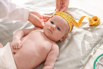 Pediatrician measuring baby's head with tape at table in clinic, closeup