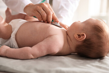 Pediatrician examining baby with stethoscope at table in clinic, closeup