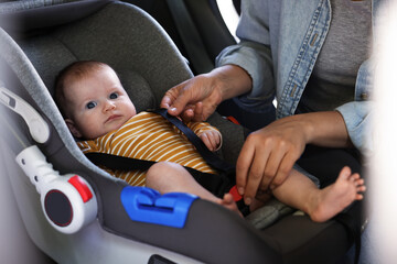 Mother fastening her baby in car seat, closeup