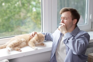 Man suffering from allergy with his cat near window at home