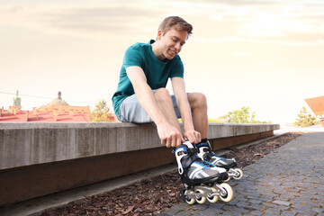 Happy man putting on roller skates outdoors