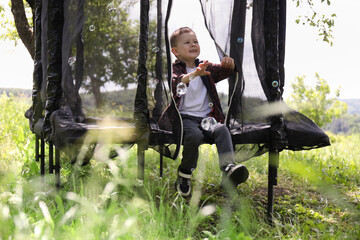 Happy boy playing with soap bubbles on trampoline outdoors