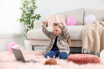 Birthday celebration. Little girl with cake having video call via laptop at home