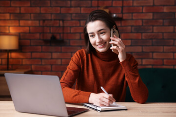 Smiling woman talking by smartphone and working at desk in home office