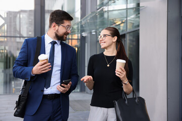 Happy coworkers with coffee discussing something near office building