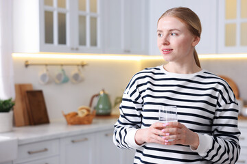 Young woman with glass of water in kitchen. Space for text