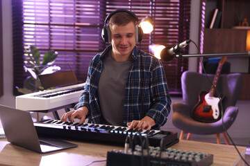 Smiling man in headphones working with MIDI keyboard at table in home studio