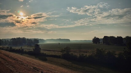 Misty Sunrise Over Open Farmland with Golden Sky and Silhouetted Trees