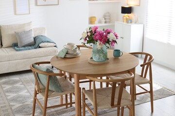 Dining table with beautiful flowers and dishware in room. Interior design
