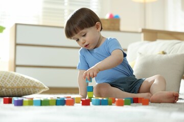 Cute little child playing with colorful cubes at home
