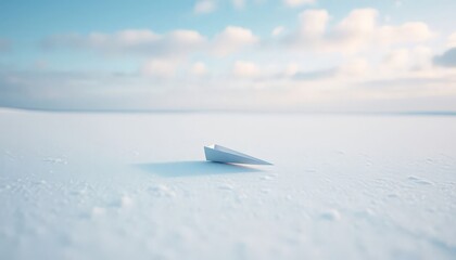 Fototapeta premium White paper airplane resting on a vast snowy plain under a clear blue sky