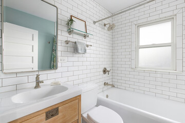 A white bathroom with subway tile walls, bronze faucets, and a natural wood cabinet with a white...