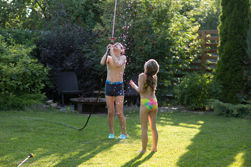 Happy children brother and sister playing in the garden hose and having fun with spray of water in...