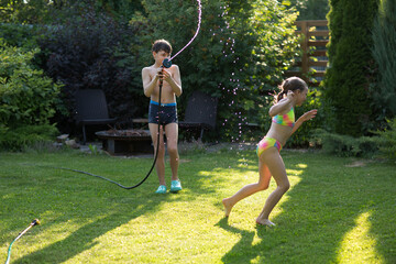 Happy children brother and sister playing in the garden hose and having fun with spray of water in...
