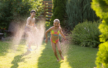 Happy children brother and sister playing in the garden hose and having fun with spray of water in...