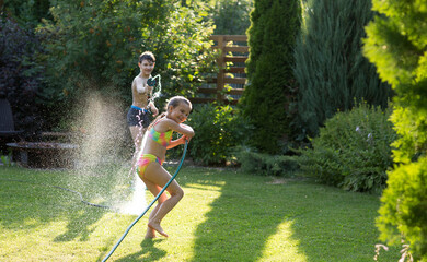 Happy children brother and sister playing in the garden hose and having fun with spray of water in...