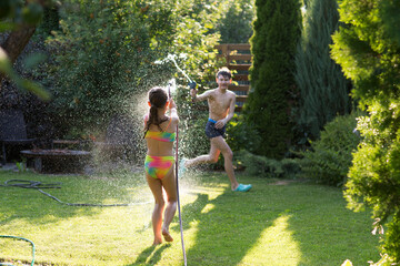 Happy children brother and sister playing in the garden hose and having fun with spray of water in...