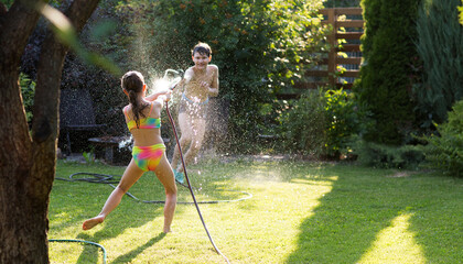 Happy children brother and sister playing in the garden hose and having fun with spray of water in...