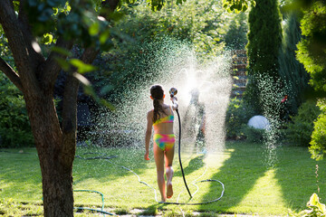 Happy children brother and sister playing in the garden hose and having fun with spray of water in...