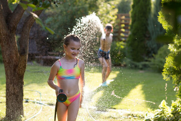 Happy children brother and sister playing in the garden hose and having fun with spray of water in...