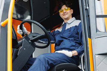 Happy driver man of industrial dump truck sits in cab and works on construction building site