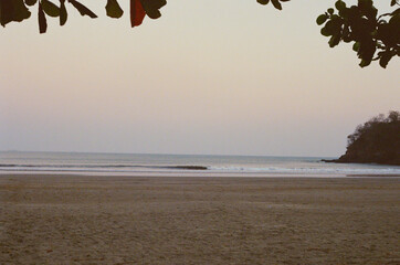 A tranquil beach during dusk, with peaceful ocean waves and a coastal view. The serene scene portrays relaxation, nature, and the gentle colors of the evening sky. Taken on 35mm Film.
