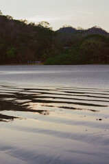 An idyllic beach scene showing rippling sands under soft twilight reflections, surrounded by lush foliage and distant hills, evoking serenity and calm with its peaceful ambiance. Taken on 35mm film