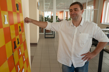 Caucasian man standing at wall mounted magnetic chessboard demonstration. 