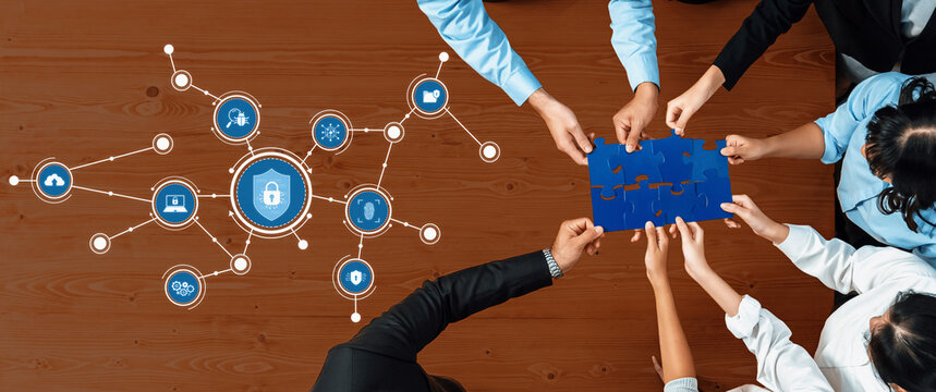 A diverse group of professionals collaborates on cybersecurity solutions, holding a puzzle piece over digital icons, symbolizing teamwork and innovation in a modern office. Amity - Powered by Adobe