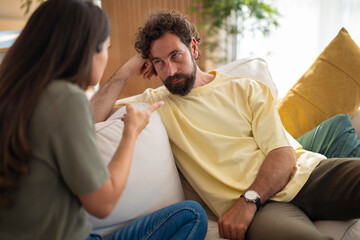 Young couple sitting on a sofa during a serious conversation. The woman is pointing while the man...