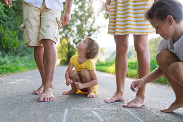 A young family with small children playing hopscotch on a road in summer.