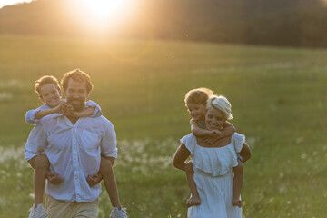 Young family with small children on walk in summer nature at sunset.