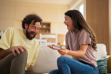 Excited young couple sitting on a couch at home, celebrating positive pregnancy test results with joyful expressions.
