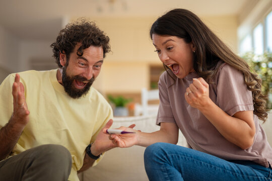 Excited young couple reacting with joy to a positive pregnancy test while sitting together on the couch at home.
- Powered by Adobe