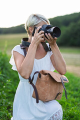 Side view of female photographer with a leather bag and camera in nature.