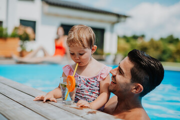 Father and young daughter drinking water while playing in pool.
