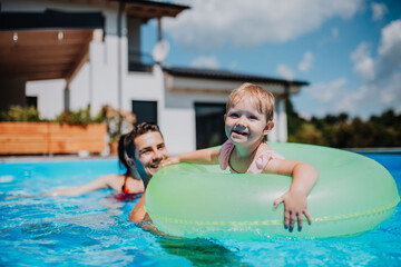 Parents and child having fun with floatie in garden swimming pool