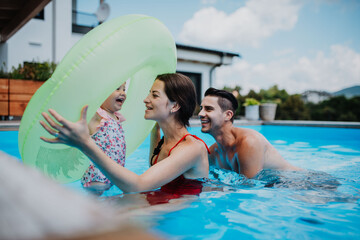 Parents and child having fun with floatie in garden swimming pool