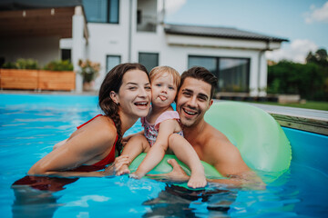 Parents and child having fun with floatie in garden swimming pool